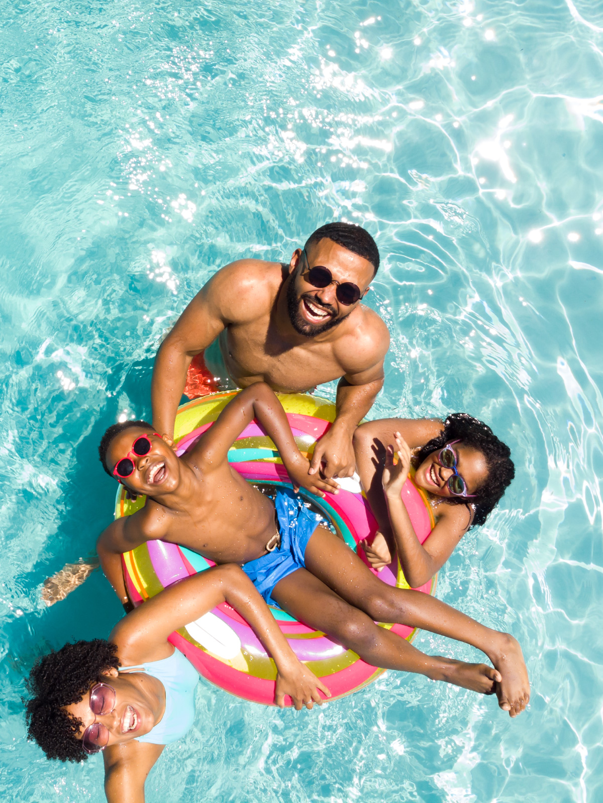 Family of four relaxing in a Best World community pool on a rainbow float